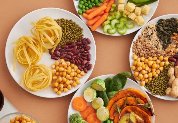 A vibrant mix of legumes, vegetables, nuts, and pasta arranged on white plates showcasing a balanced, healthy diet.